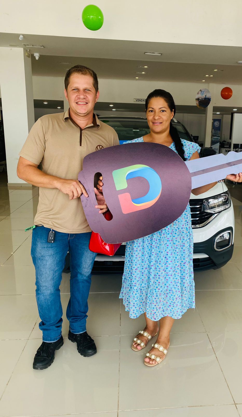Casal com chave simbólica diante de um veículo
